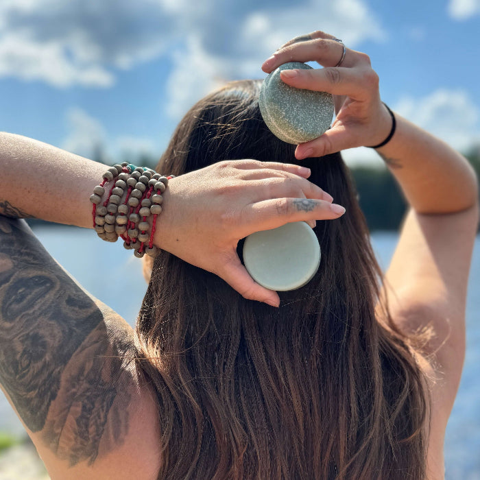 Person with tattoos using a hairbrush outdoors with a blue sky background